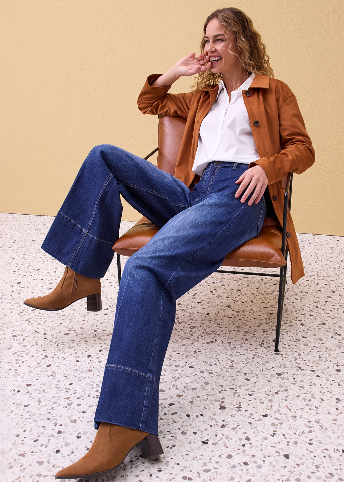 Braune Lederjacke, weißes Hemd und weit geschnittene Jeans.